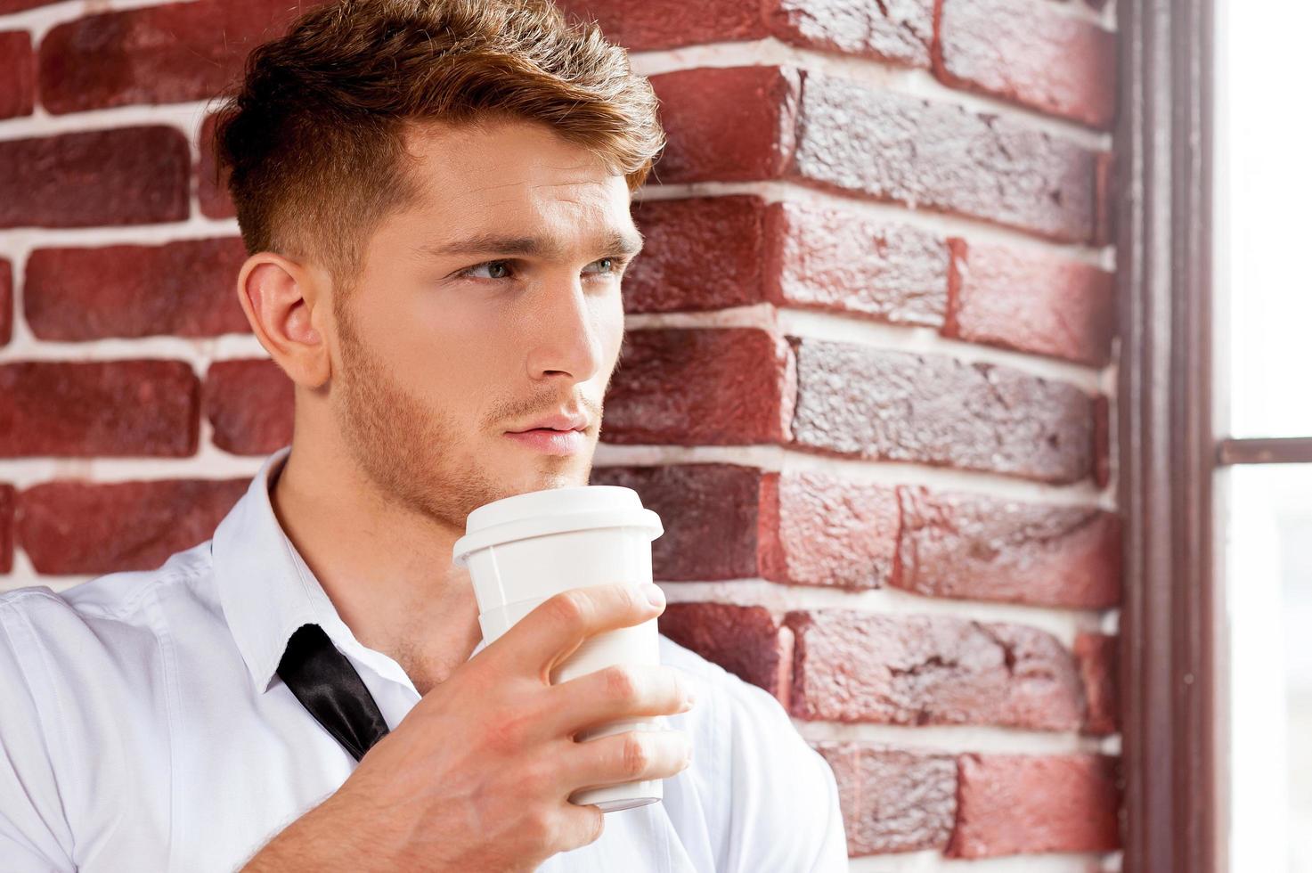 en busca de nuevas ideas creativas. apuesto joven con camisa y corbata sosteniendo una taza de café y mirando por la ventana foto