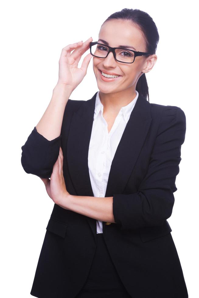 Confident and successful. Confident young woman in formalwear adjusting her eyeglasses and looking at camera while standing isolated on white photo