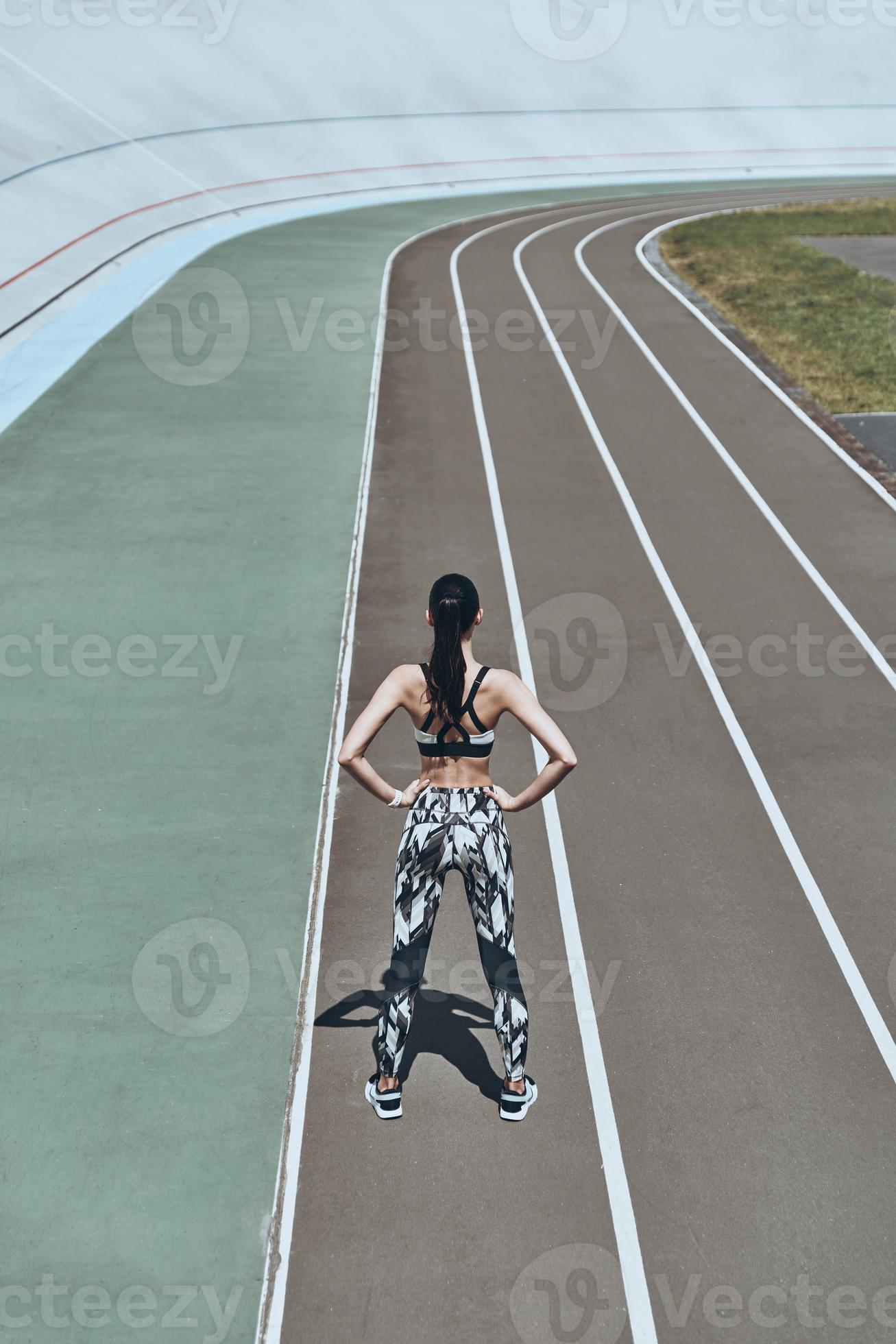 Woman athlete in fitness attire standing on running track with