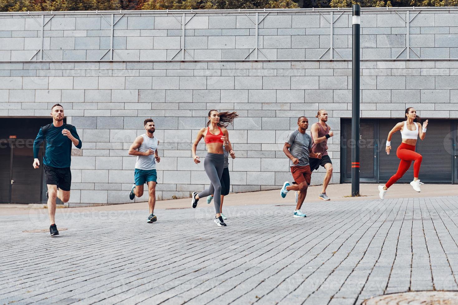 Full length of young people in sports clothing jogging while exercising outdoors photo