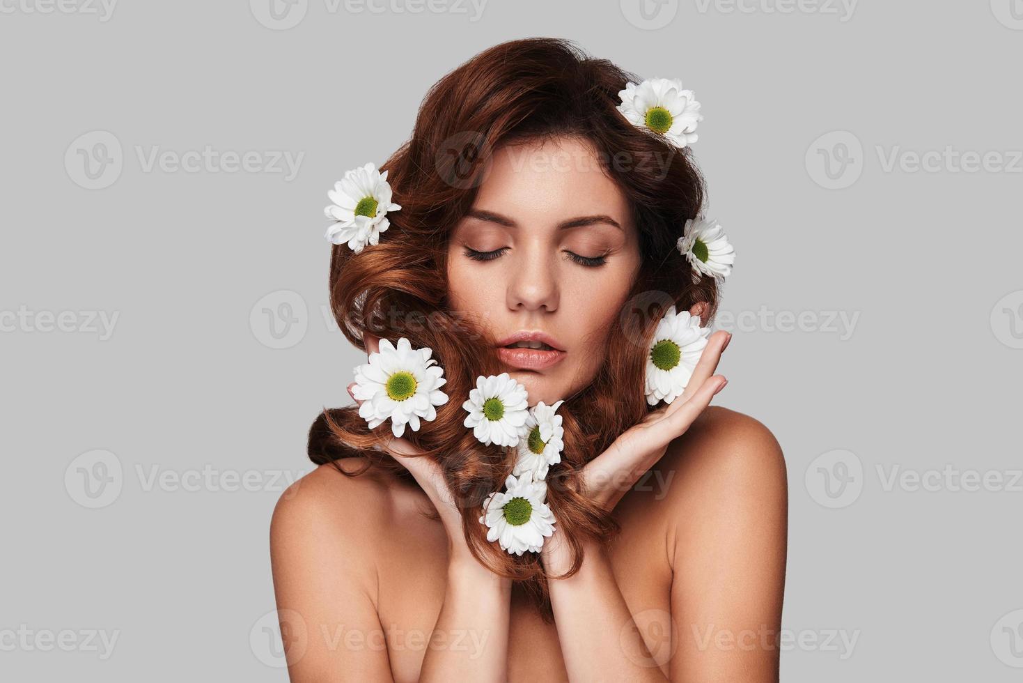 sintiéndose tan natural y atractiva mujer joven manteniendo los ojos cerrados y tocándose el pelo mientras está de pie contra un fondo gris foto