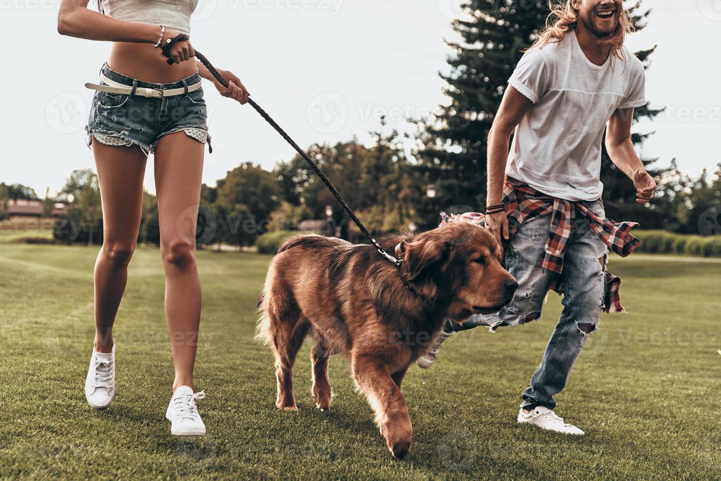 Feeling free and happy. Close-up of young modern couple playing with their dog while running in the park photo