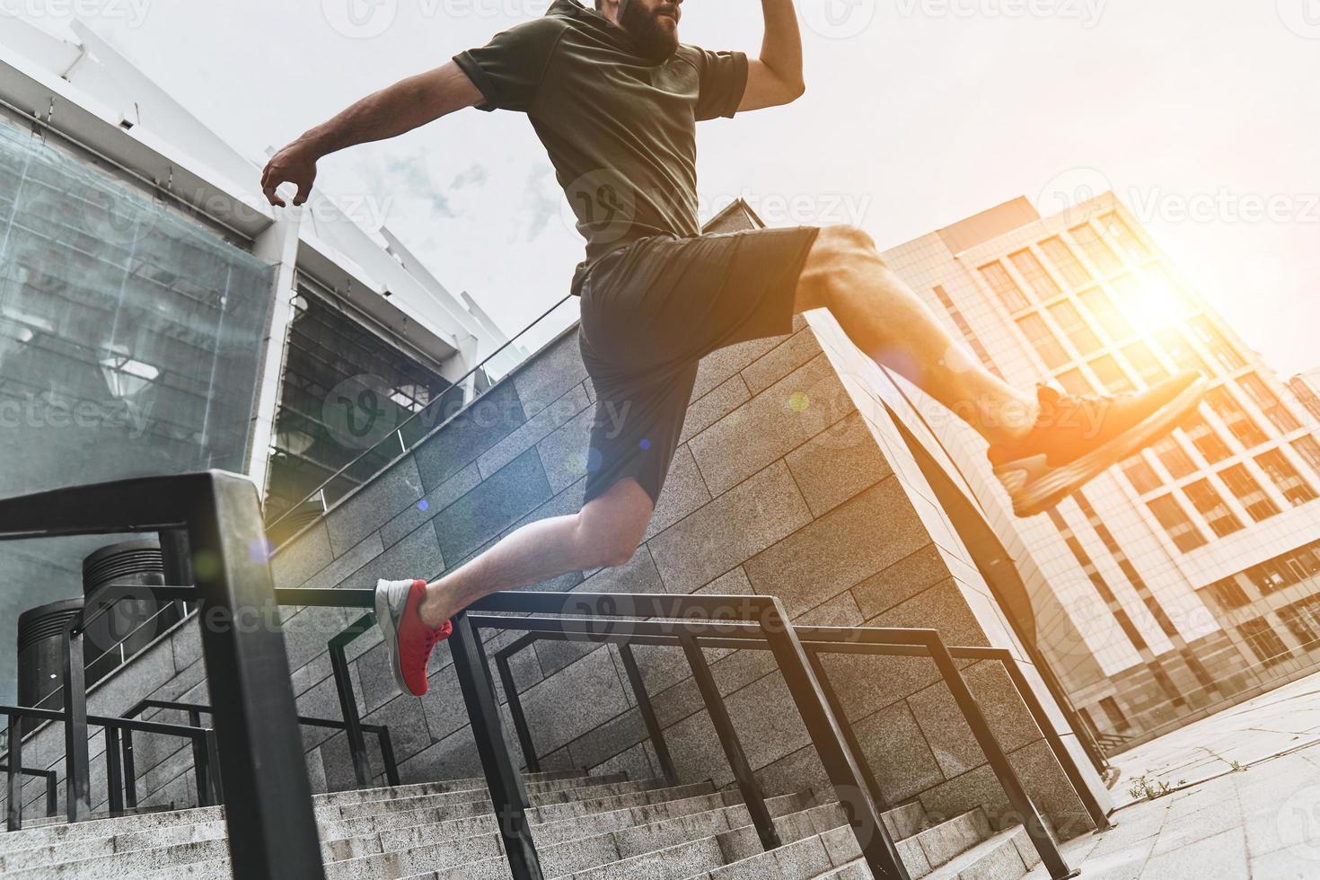 Man in the mid-air. Low angle view of young man in sport clothing jumping while exercising outside photo