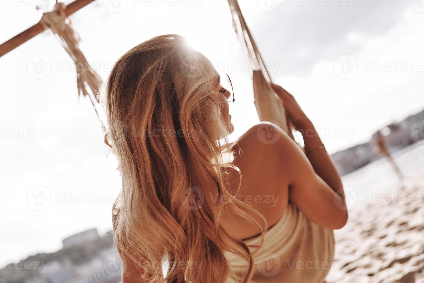 Simple joy. Rear view of attractive young woman in swimwear sunbathing while sitting in the hammock on the beach photo