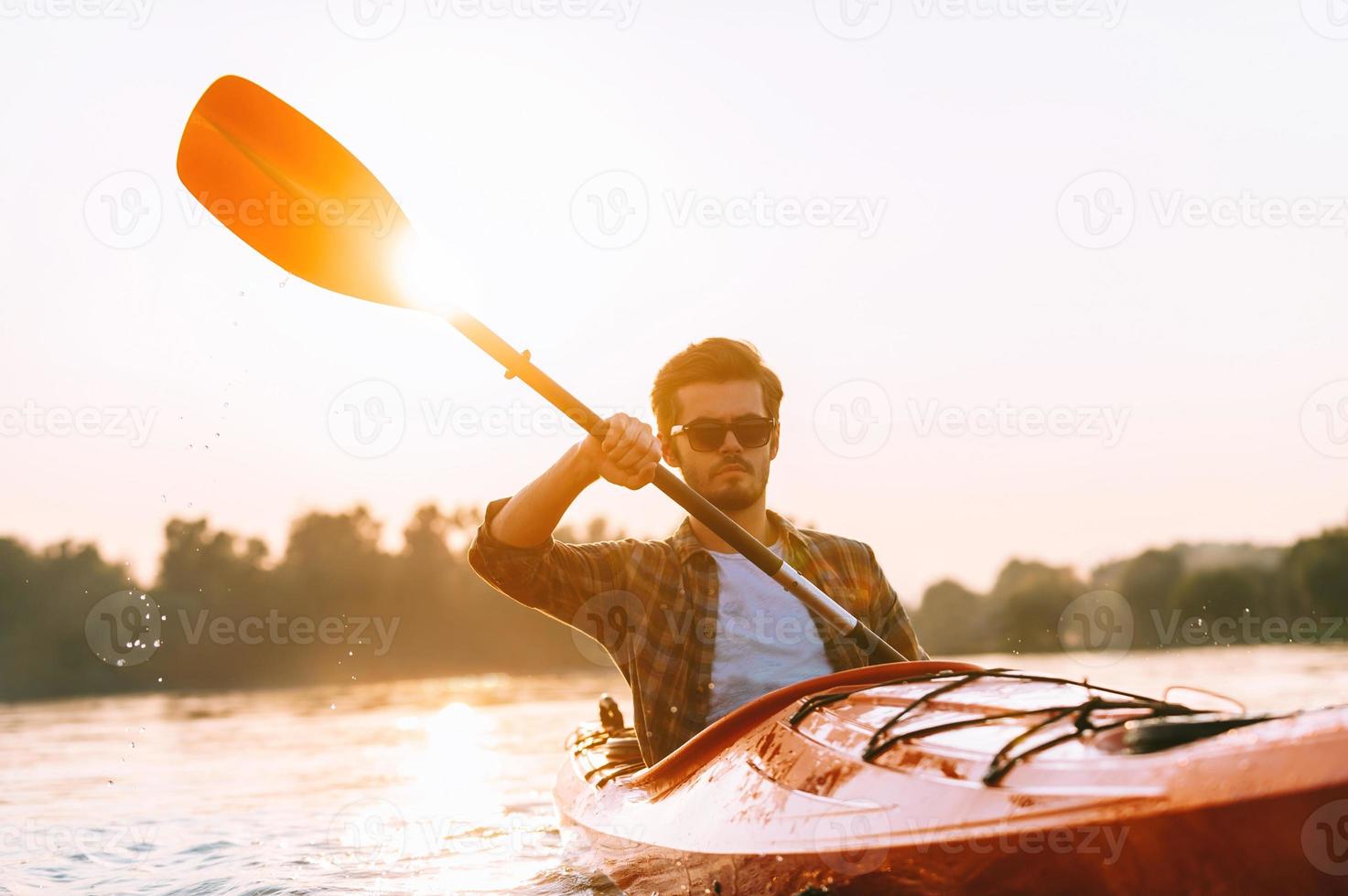Man kayaking. Handsome young man kayaking on river with sunset in the background photo