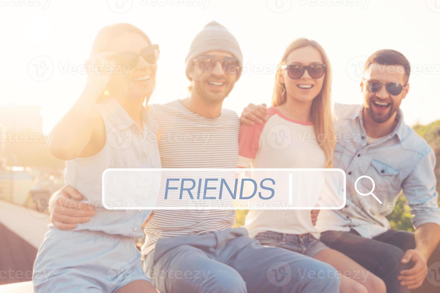 Best friends. Four young cheerful people bonding to each other and smiling while sitting on the roof of the building together photo