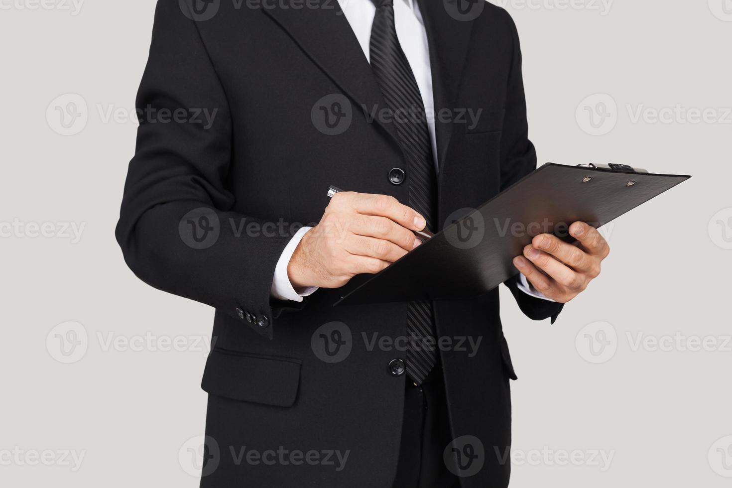 Making notes. Cropped image of man in formalwear keeping arms crossed and smiling while standing against grey background photo