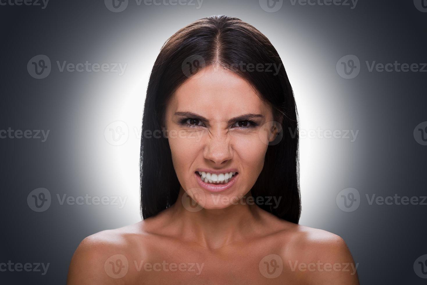 Furious beauty. Portrait of furious young shirtless woman looking at camera and grimacing while standing against grey background photo