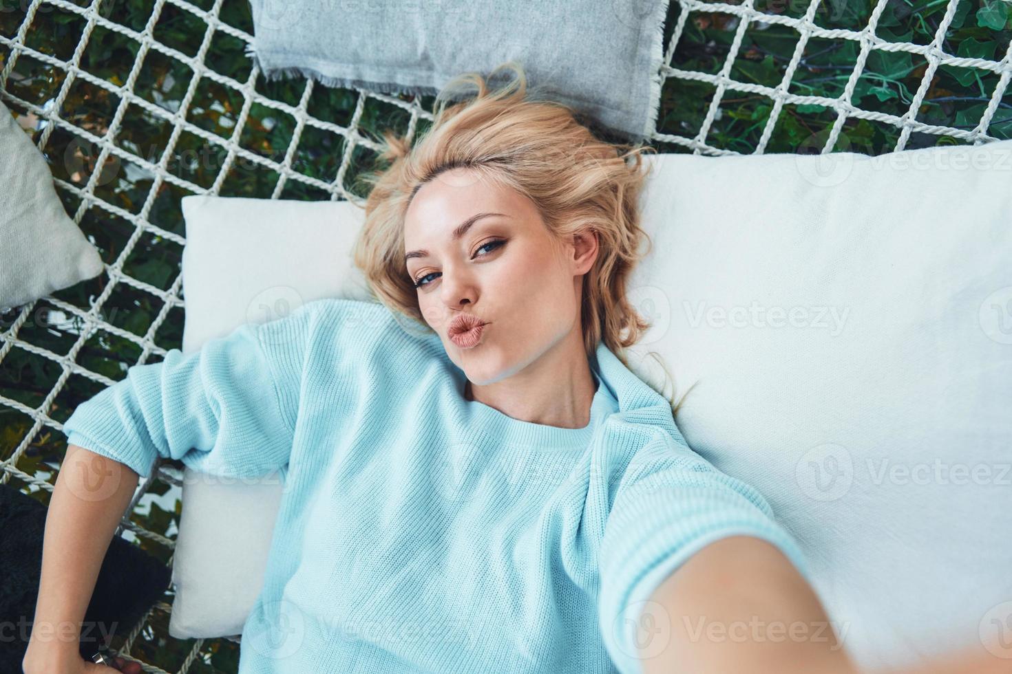 Top view of beautiful young woman making selfie while relaxing in big hammock photo