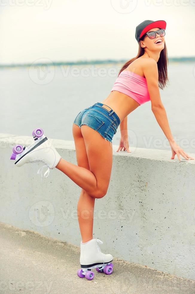 Sporty beauty. Beautiful young smiling woman in roller skates leaning at the parapet and lifting her leg up photo