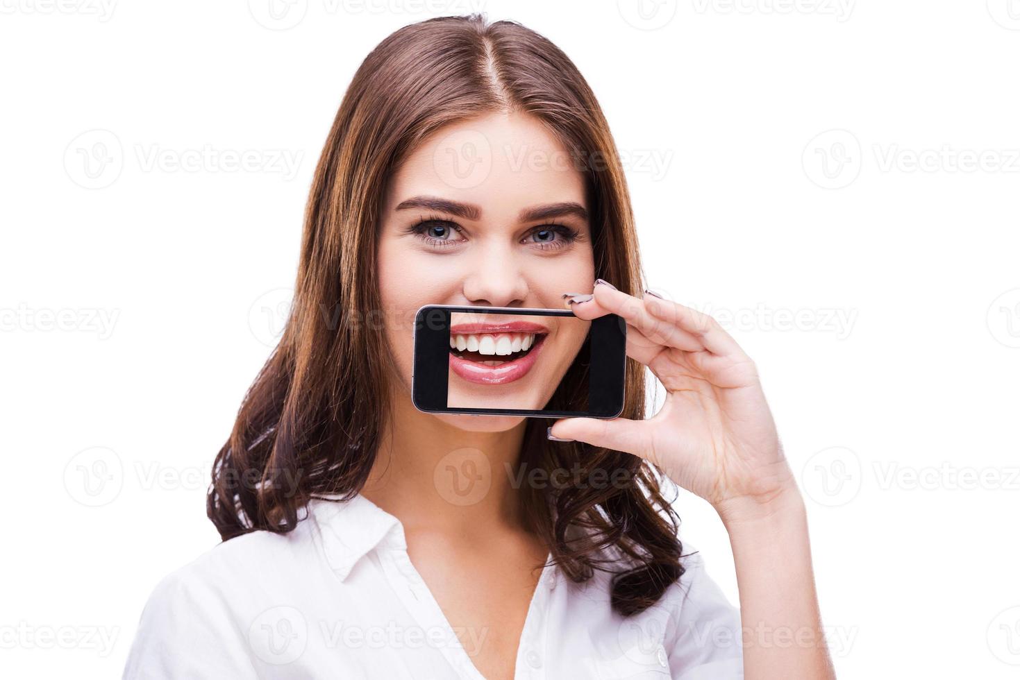 sonrisa sincera hermosas mujeres jóvenes sosteniendo el teléfono móvil contra su boca y sonriendo mientras están de pie contra el fondo gris foto