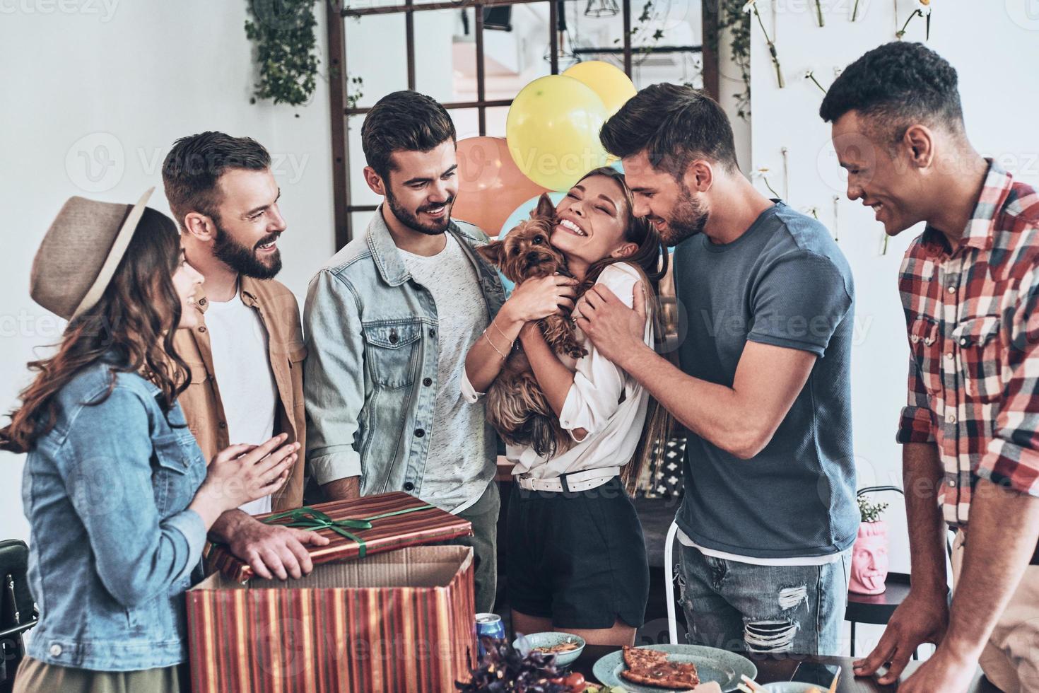 mejor sorpresa de cumpleaños. mujer joven feliz sosteniendo un cachorro y sonriendo mientras sus amigos están de pie alrededor foto