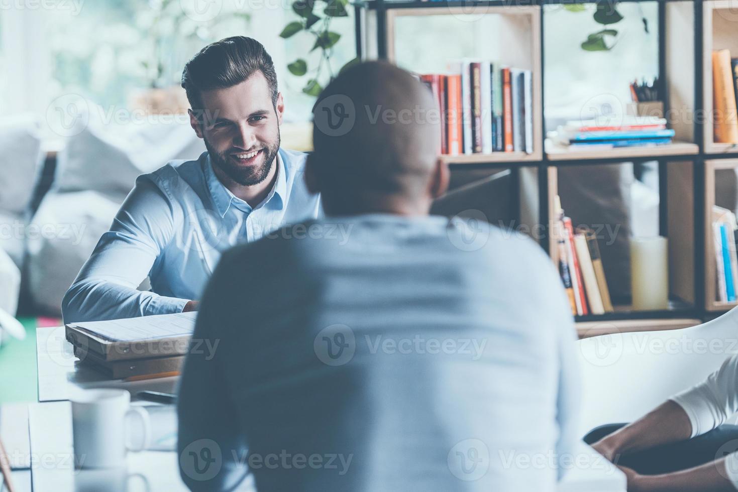 Job interview. Two young men in smart casual wear sitting at the office desk together while one of them smiling photo