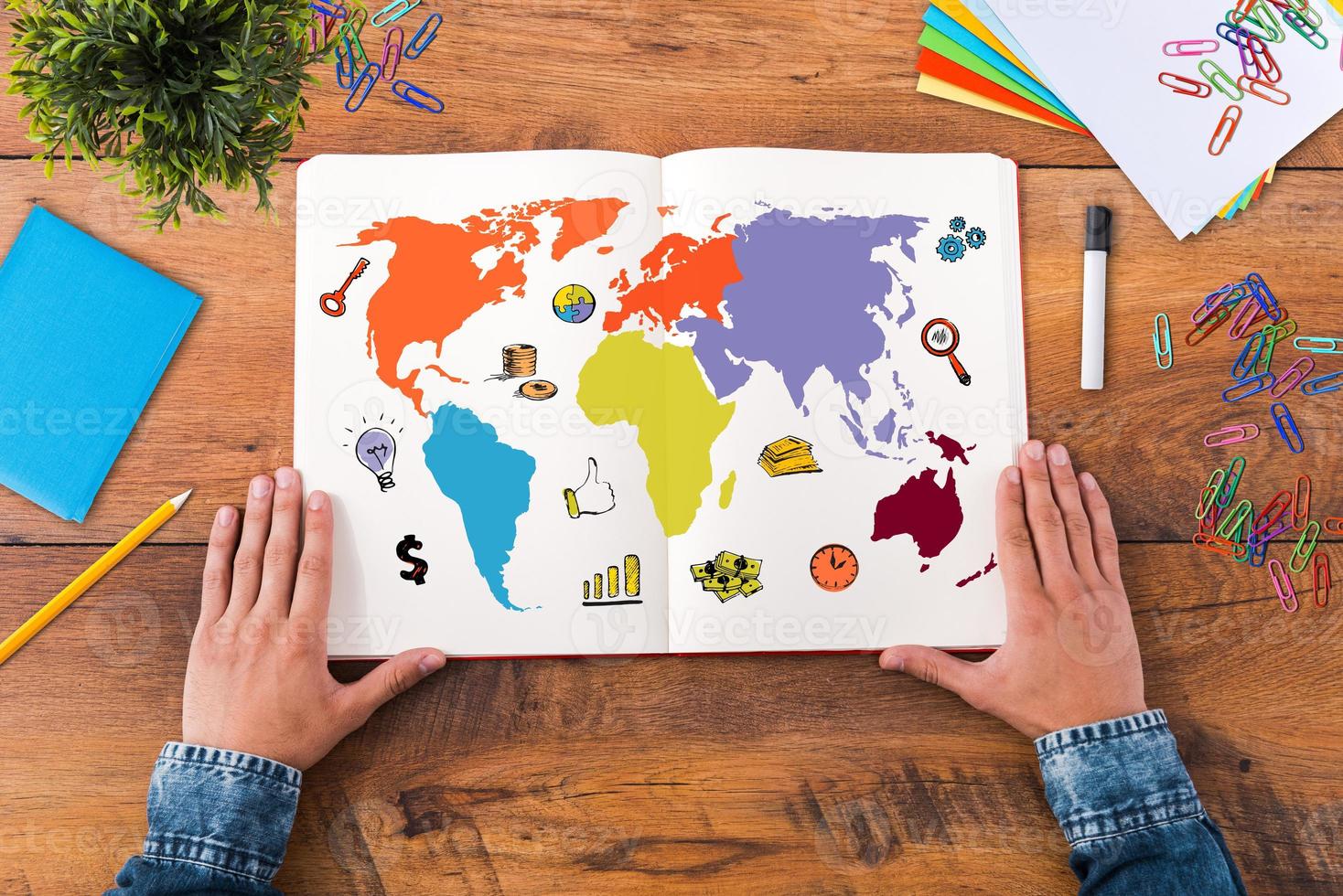 Planning his journey. Top view close-up image of man holding hands on his notebook with colorful map on it while sitting at the wooden desk photo