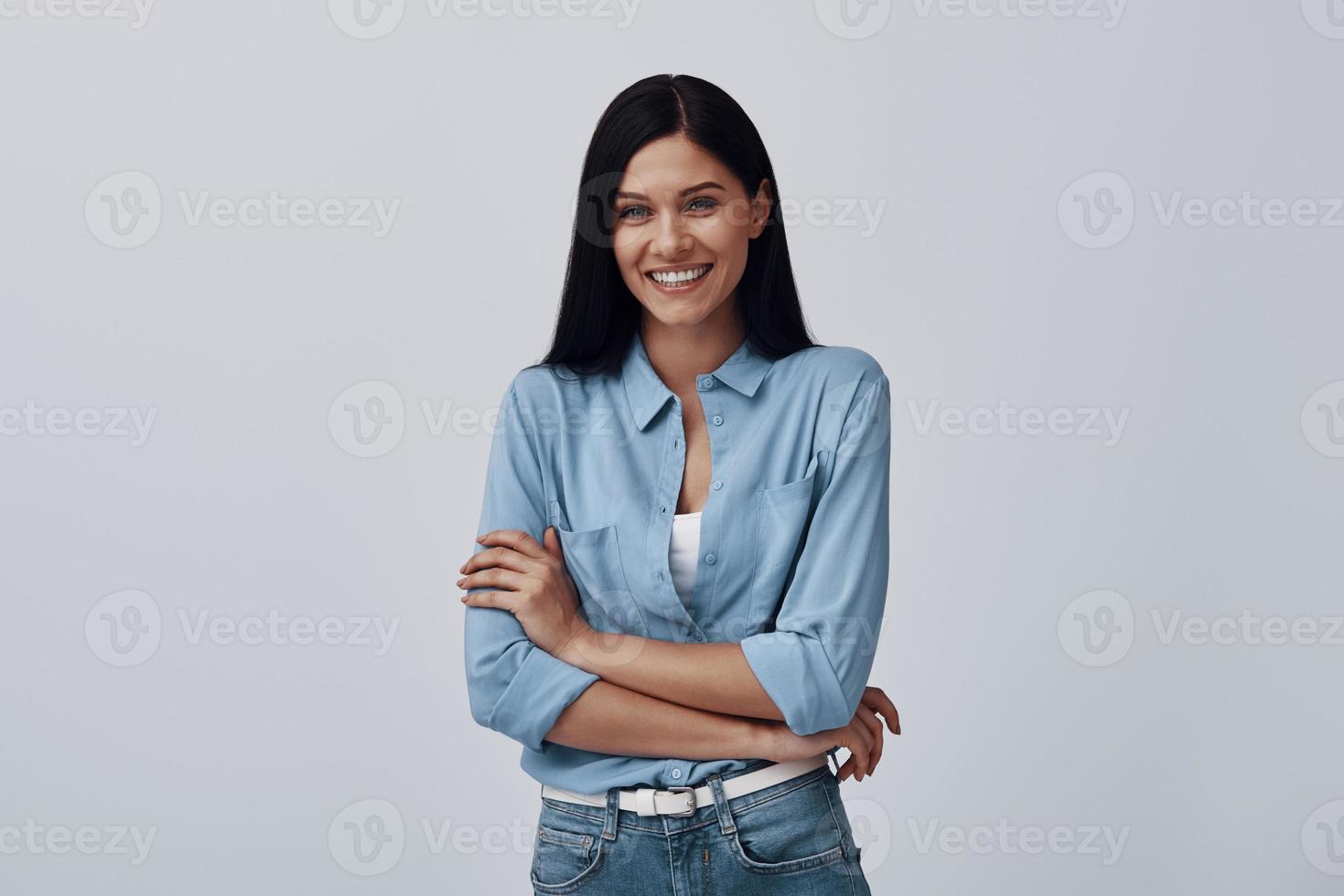 Attractive young woman looking at camera and smiling while standing against grey background photo