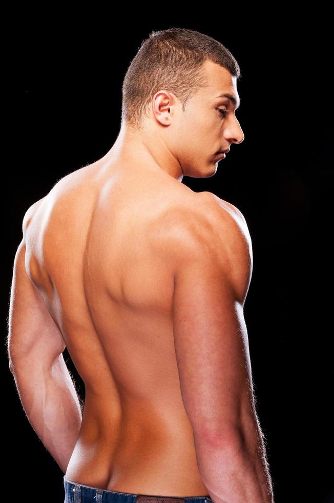 Muscular handsome. Rear view of young muscular man standing against black background photo