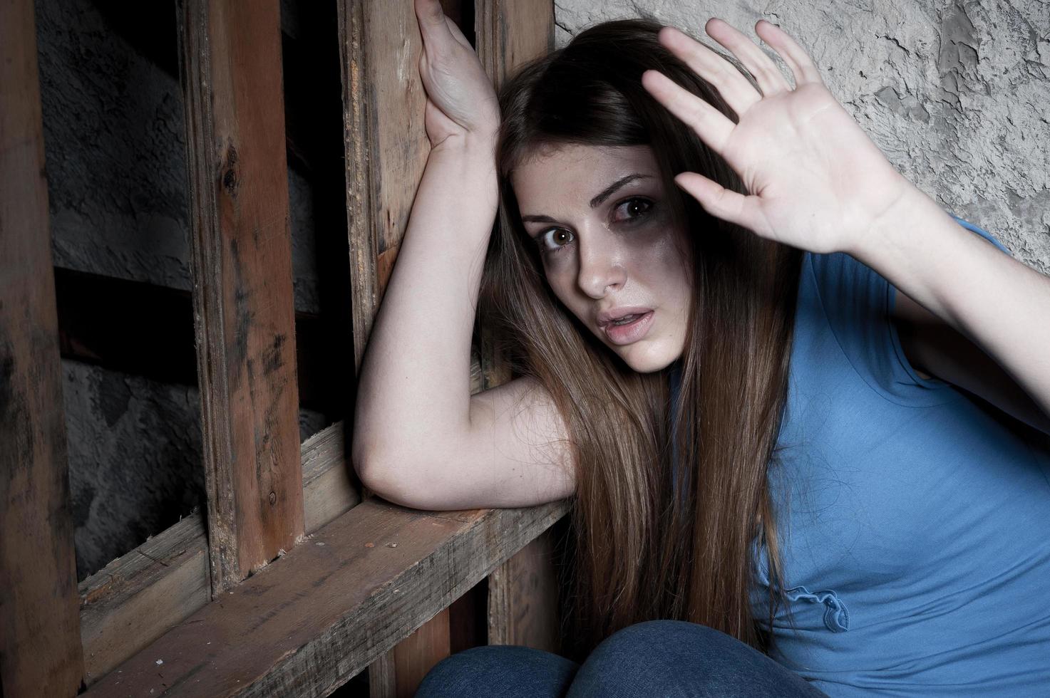 sorprendido y aterrorizado. mujer joven aterrorizada mirando a la cámara y estirando la mano mientras se apoya en la pared oscura foto