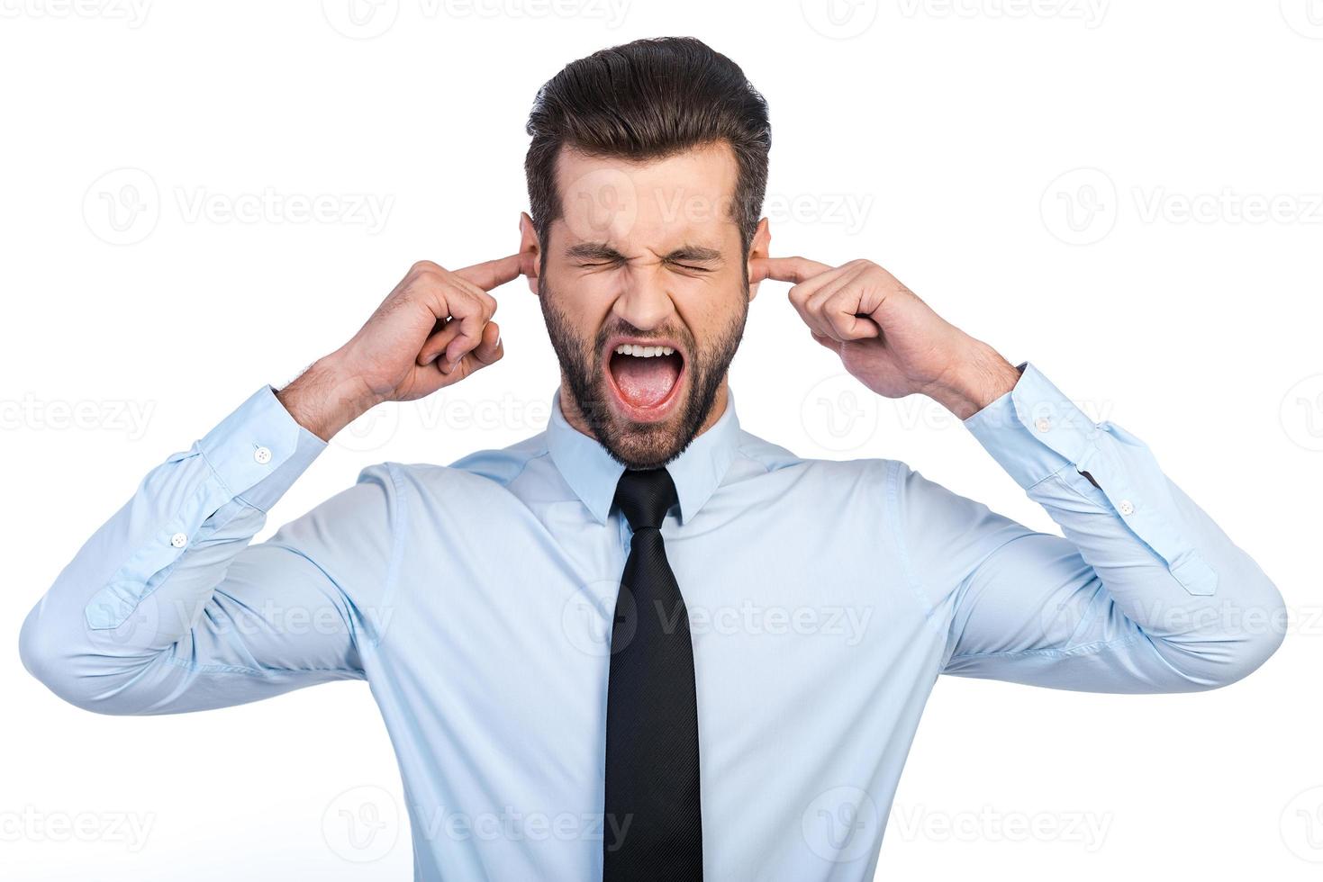 Too loud sound  Frustrated young man in shirt and tie covering ears with fingers and keeping eyes closed while standing against white background photo