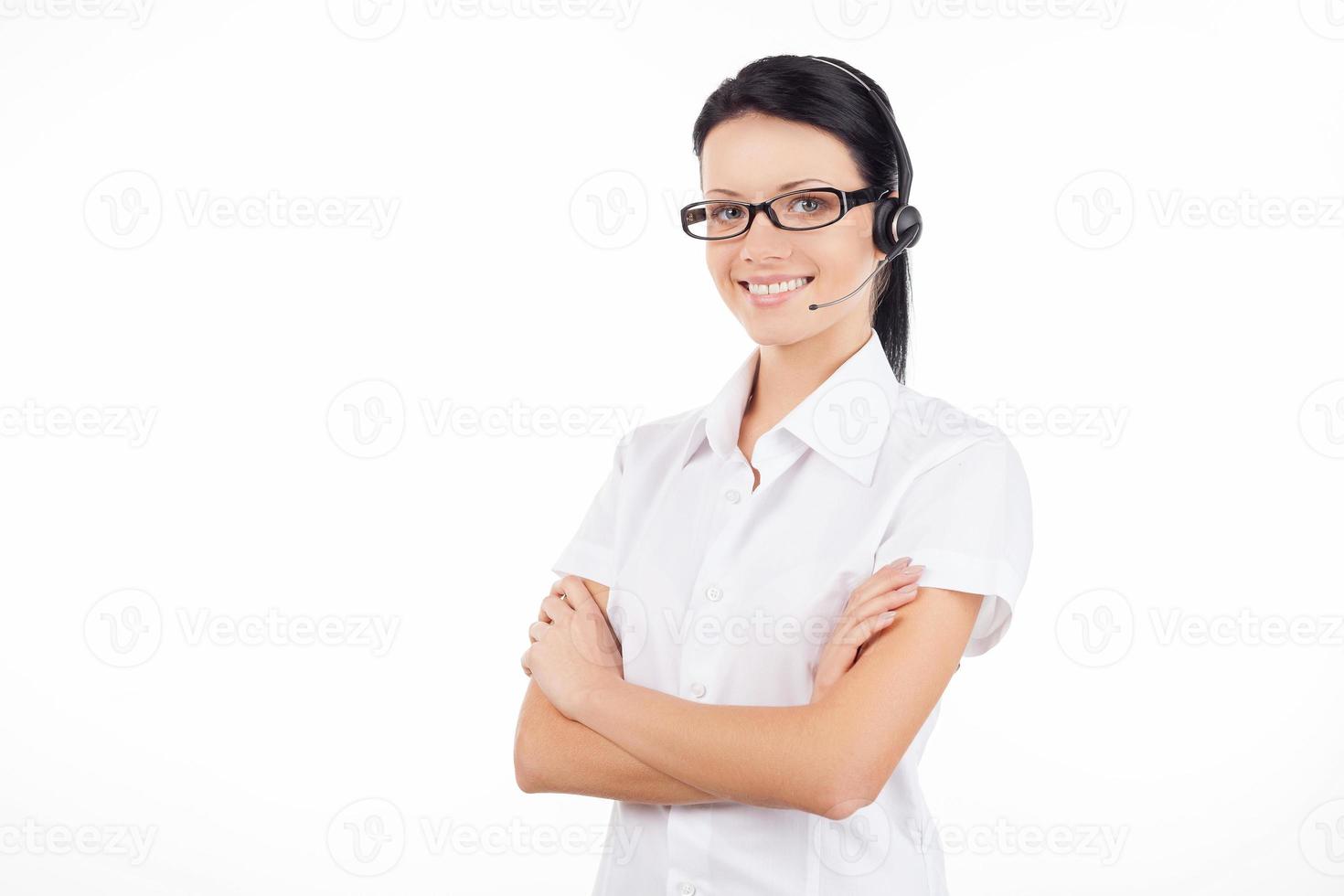 Customer service representative. Confident young woman in headset smiling and keeping her arms crossed while standing isolated on white photo