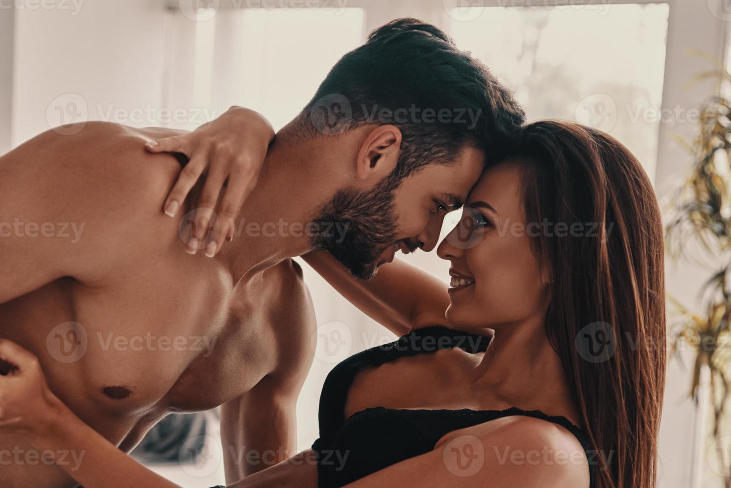 Falling in love. Beautiful young couple embracing and smiling while standing face to face in the bedroom photo