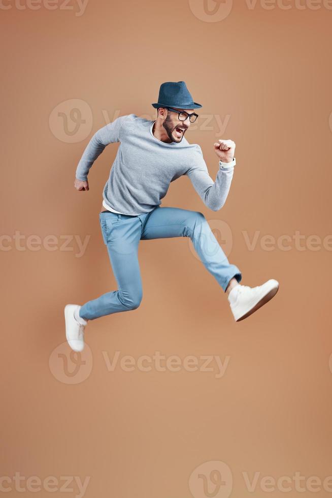 Full length of playful young man in casual wear shouting and gesturing while hovering against brown background photo