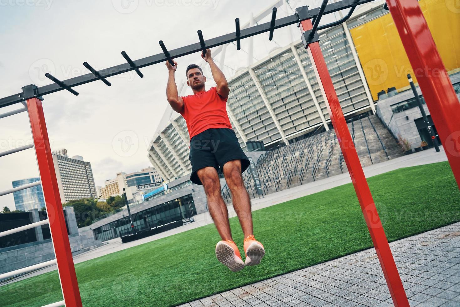 Full length of determined to win young man in sports clothing doing pull ups while exercising outdoors on the city street photo