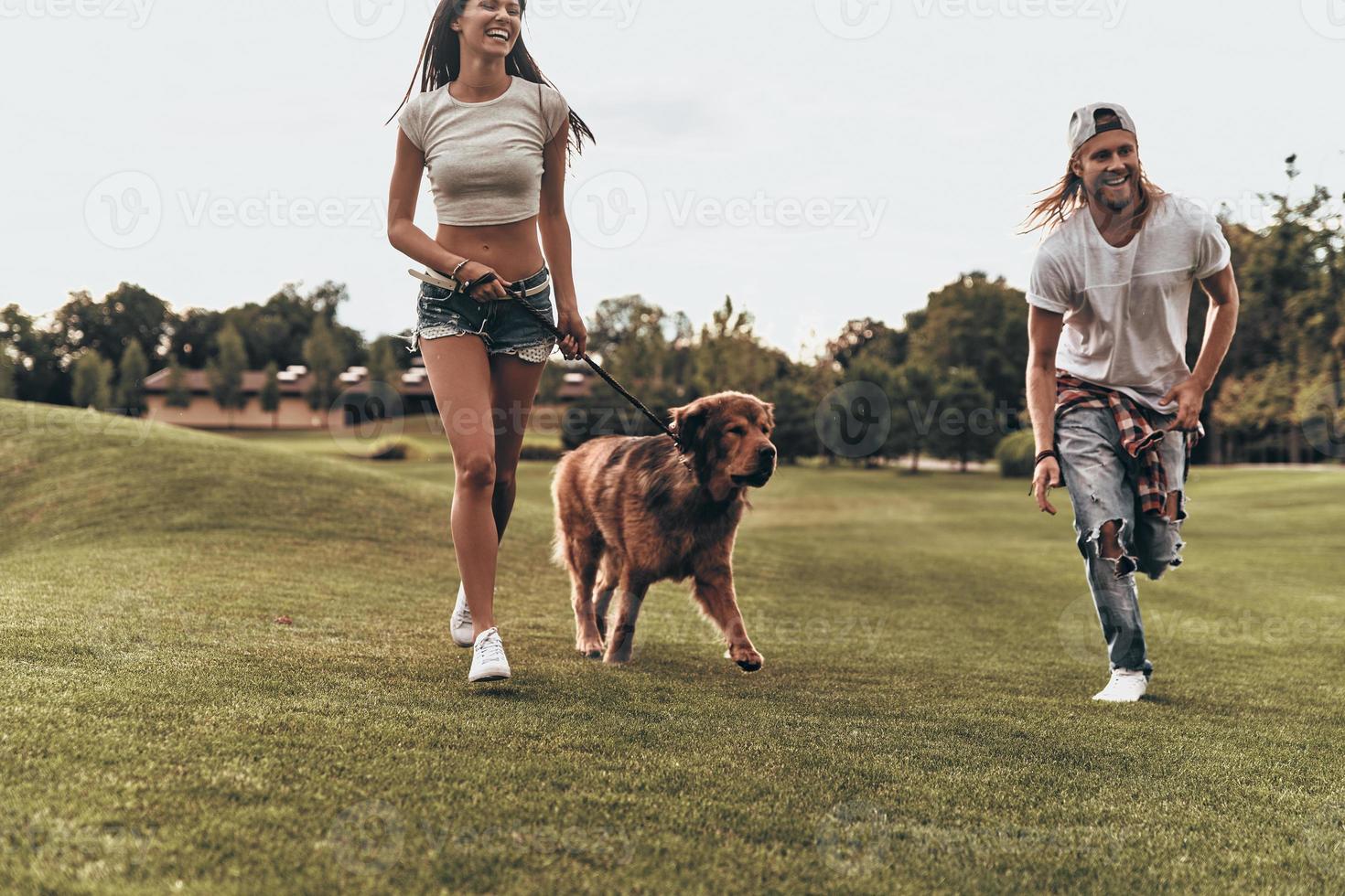 Happy to be together.  Full length of beautiful young couple playing with their dog while running in the park photo