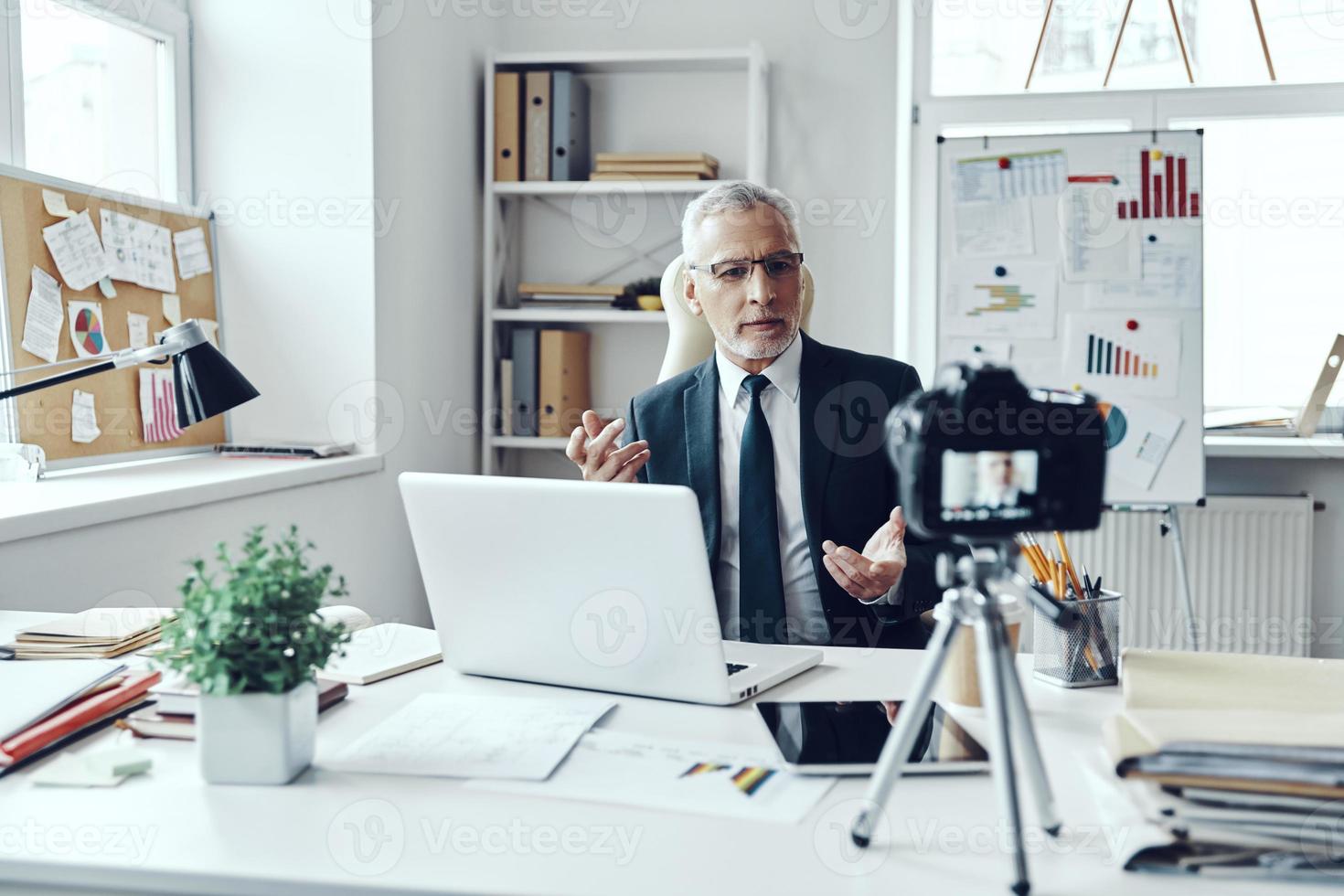 Senior man in elegant shirt and tie working using laptop while making social media video photo