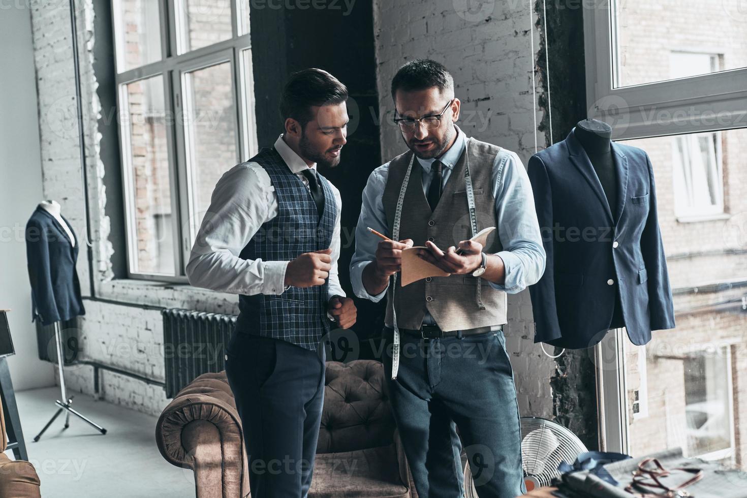 Making a list of requirements. Two young fashionable men having a discussion while standing in workshop photo
