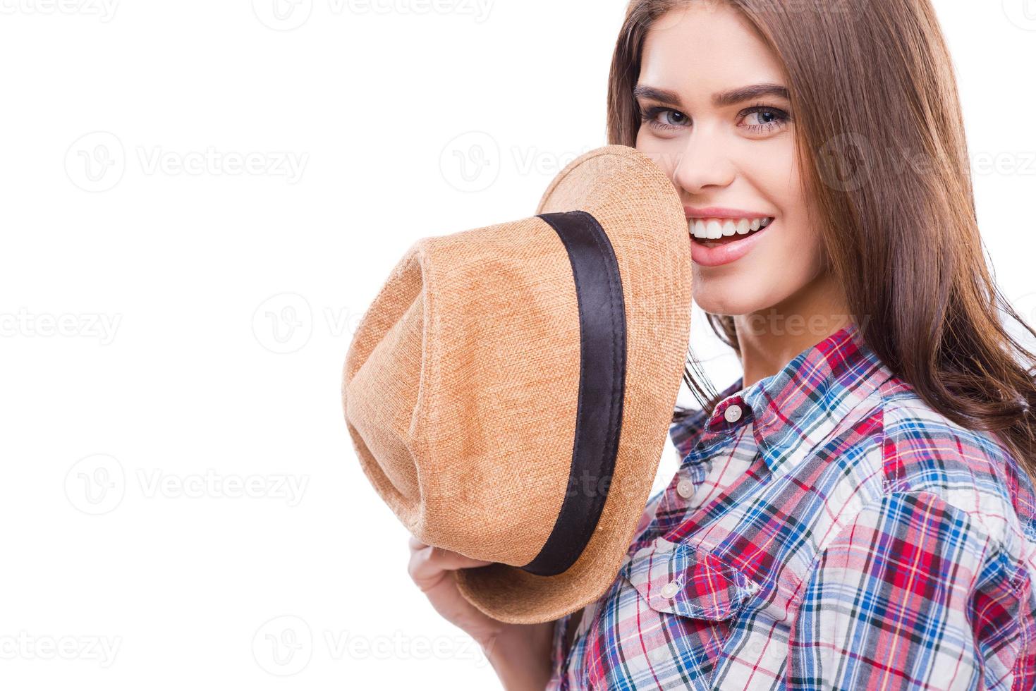 Funky beauty. Beautiful young woman in funky wear holding hat and smiling while standing against white background photo