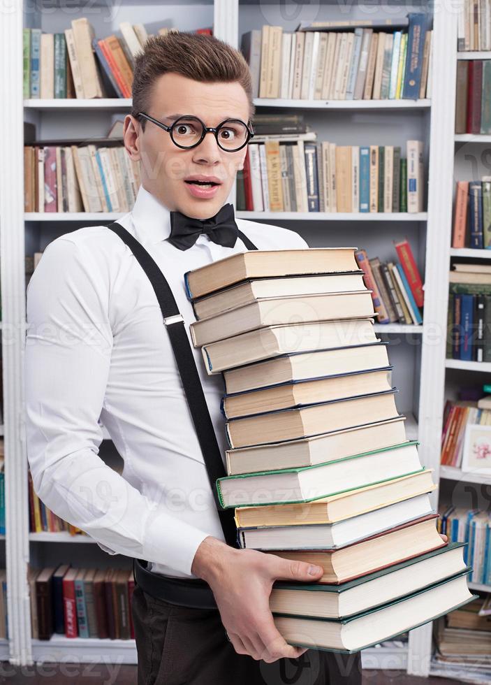 Carrying a book stack. Shocked young man in shirt and bow tie carrying a heavy book stack and looking at camera photo