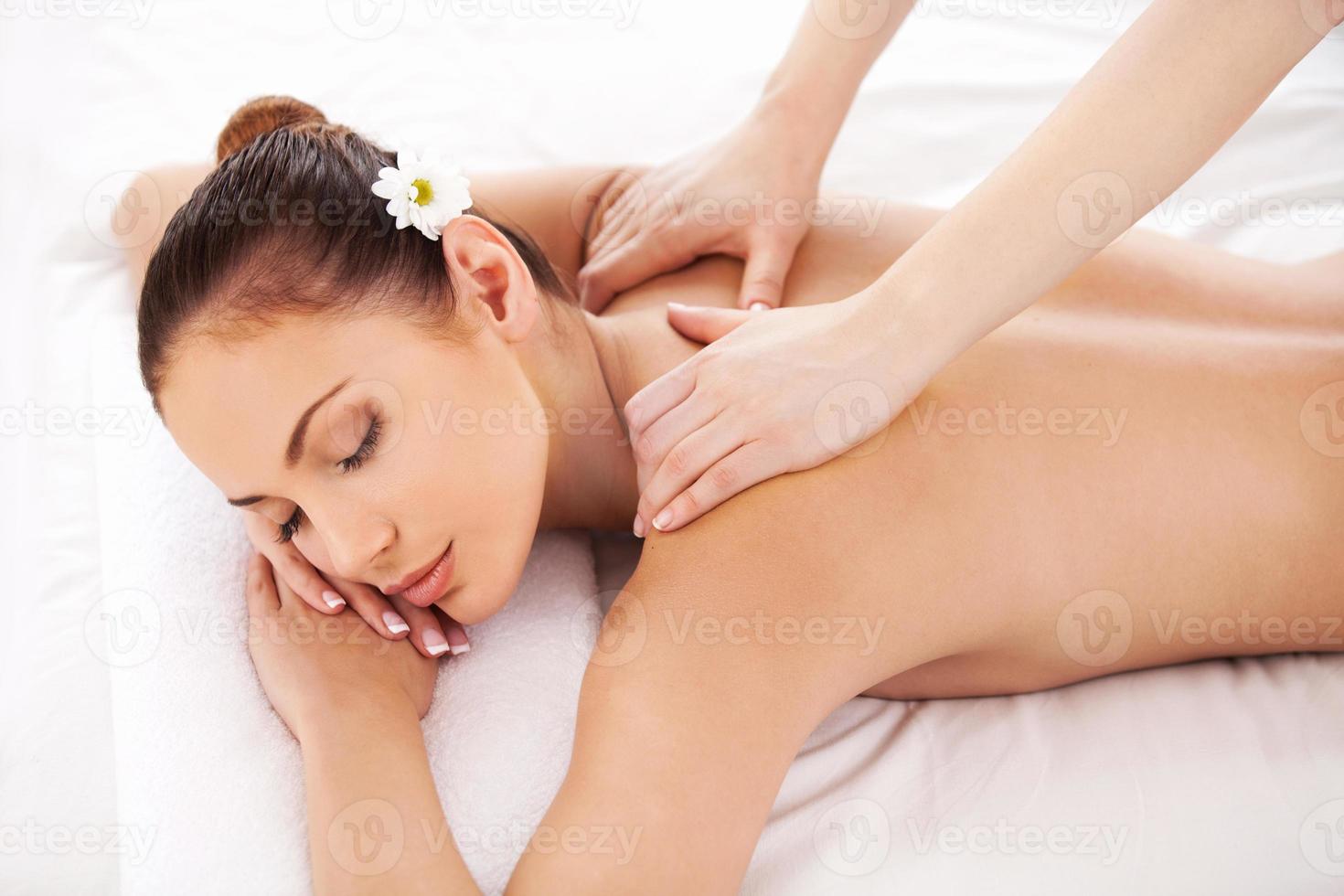 masaje para músculos cansados. vista superior de una hermosa joven acostada en la mesa de masajes y manteniendo los ojos cerrados mientras el masajista masajea sus hombros foto