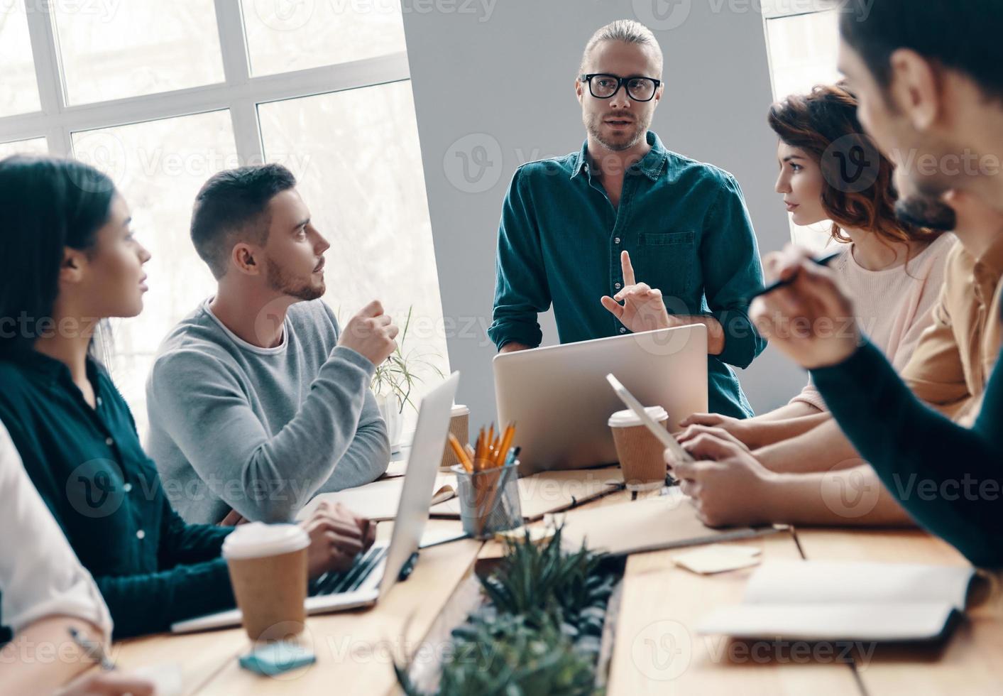 Developing new project. Group of young modern people in smart casual wear discussing something while working in the creative office photo