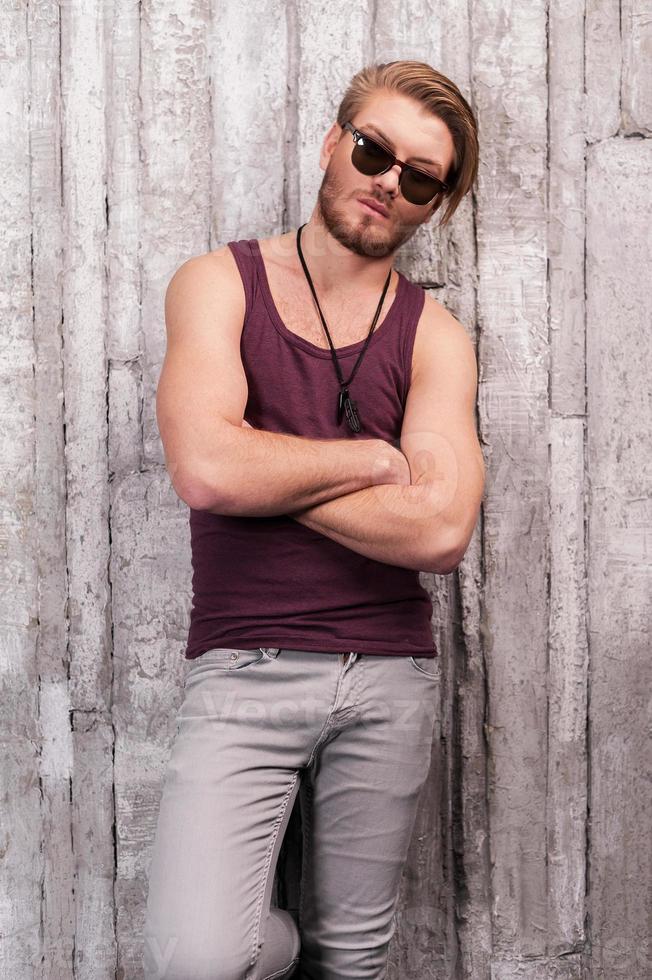 Looking trendy. Handsome young man in sunglasses leaning at the wall and looking at camera photo