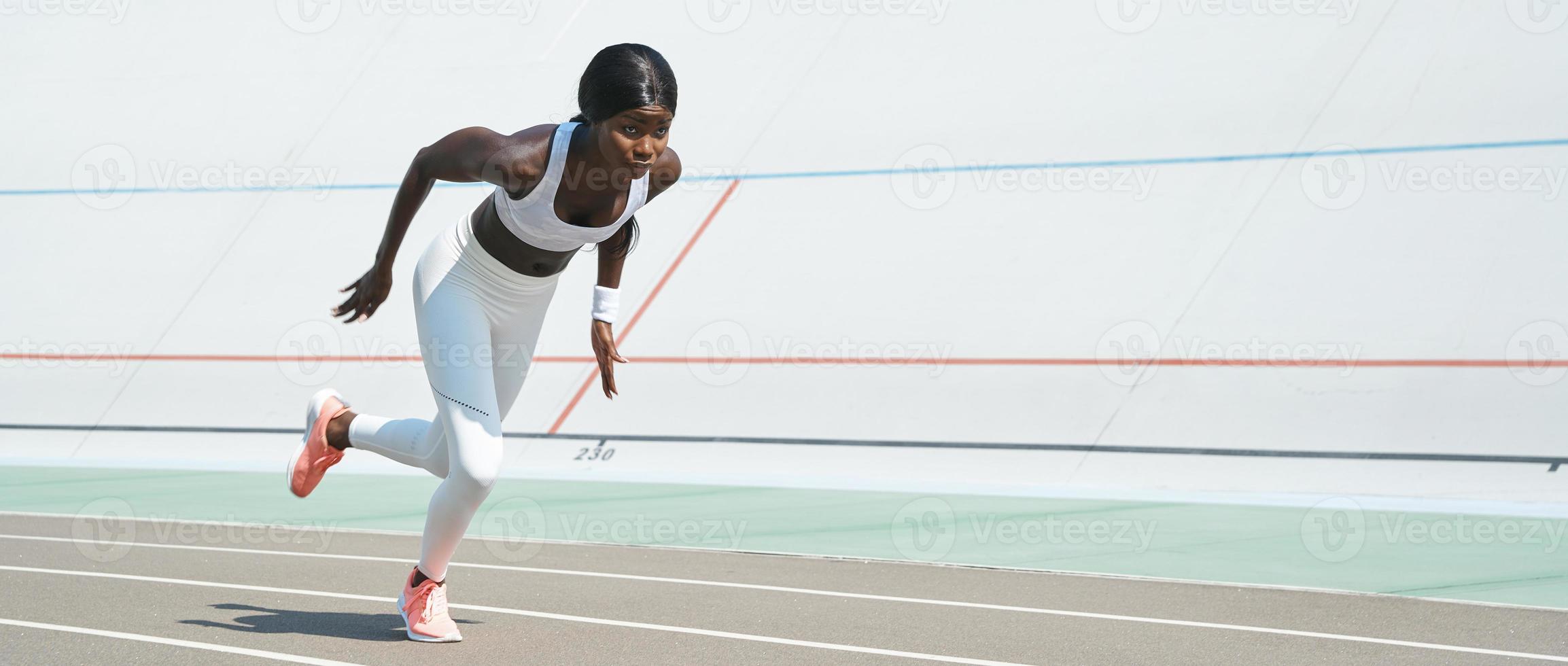 Confident young African woman in sports clothing running on track outdoors photo