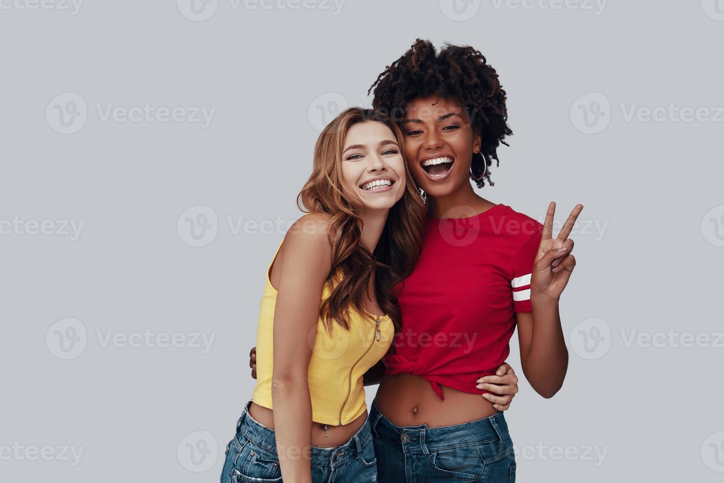 Two attractive young women looking at camera and smiling while standing against grey background photo