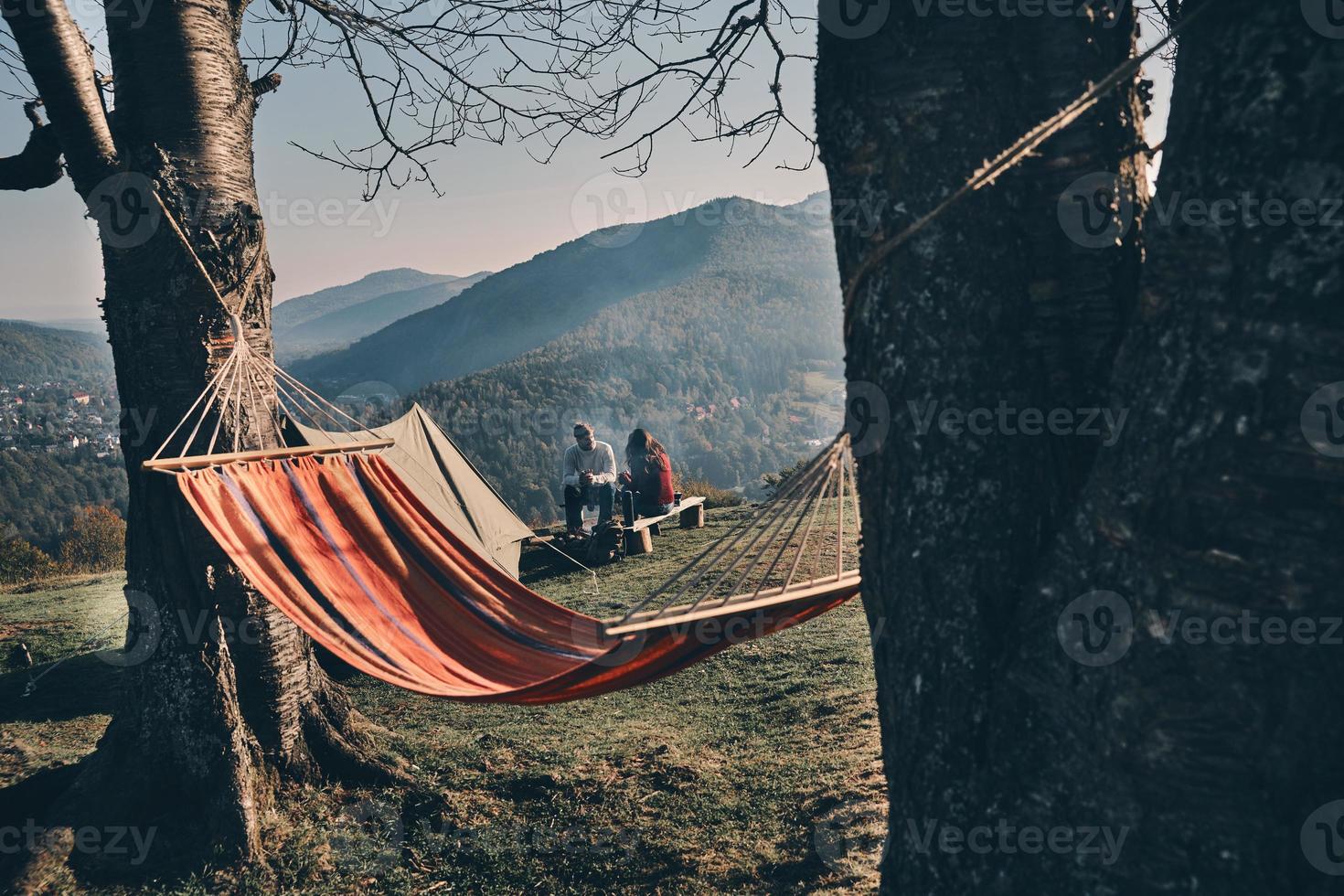 No rush. Young couple having breakfast while sitting by the campfire in mountains photo