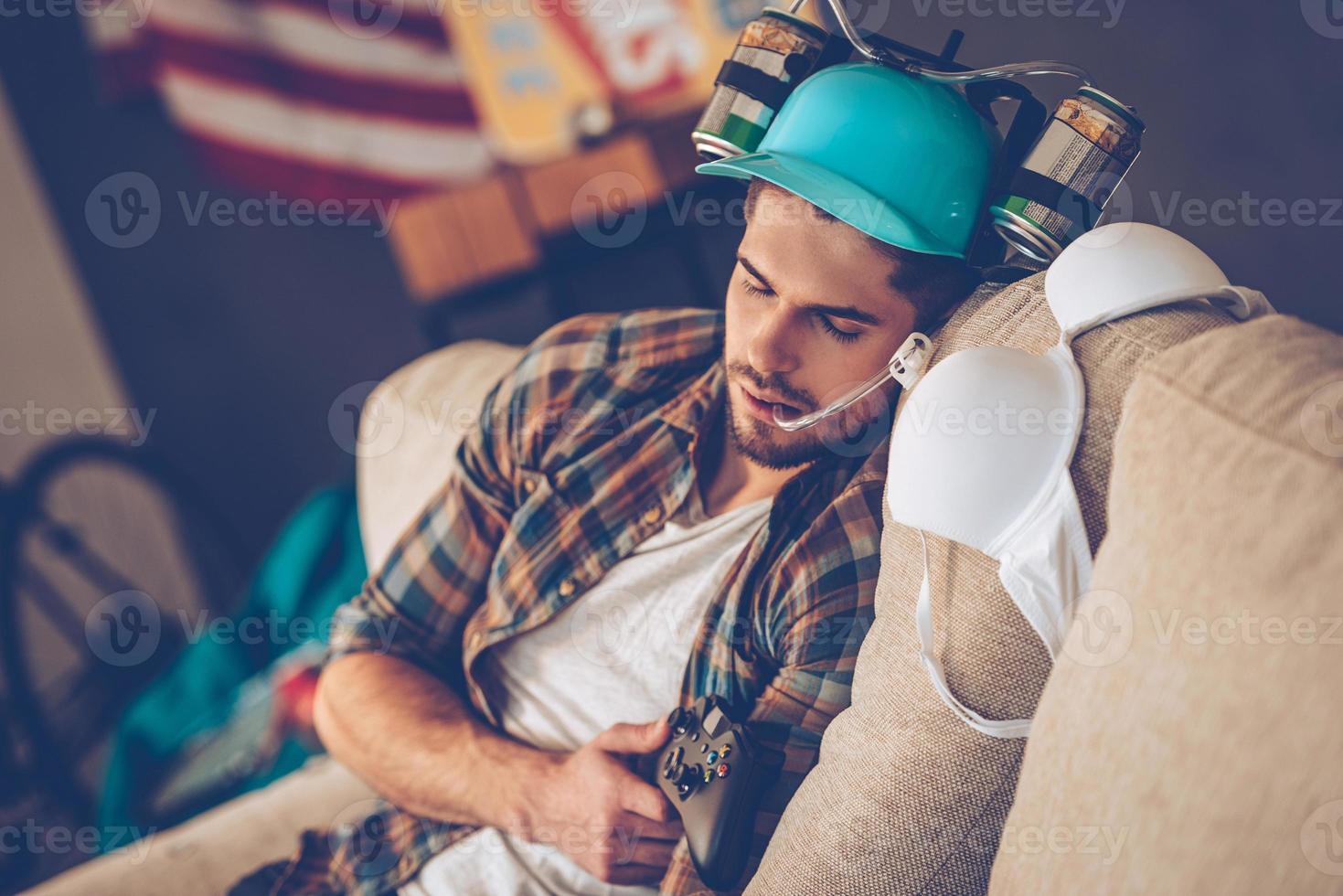 Passed out after great party. Young handsome man in beer hat napping on sofa in messy room after party photo