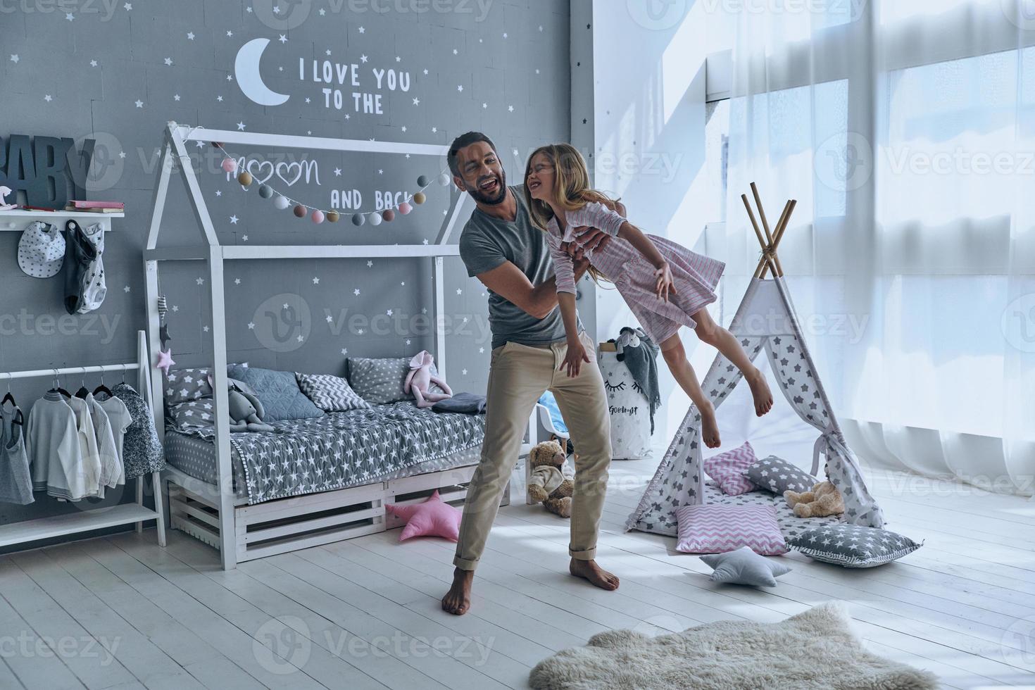 He makes her fly. Full length of father carrying his daughter and smiling while spending free time at home photo