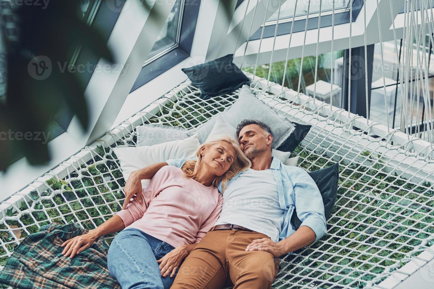 Top view of beautiful mature couple sleeping while lying down in big hammock at home together photo