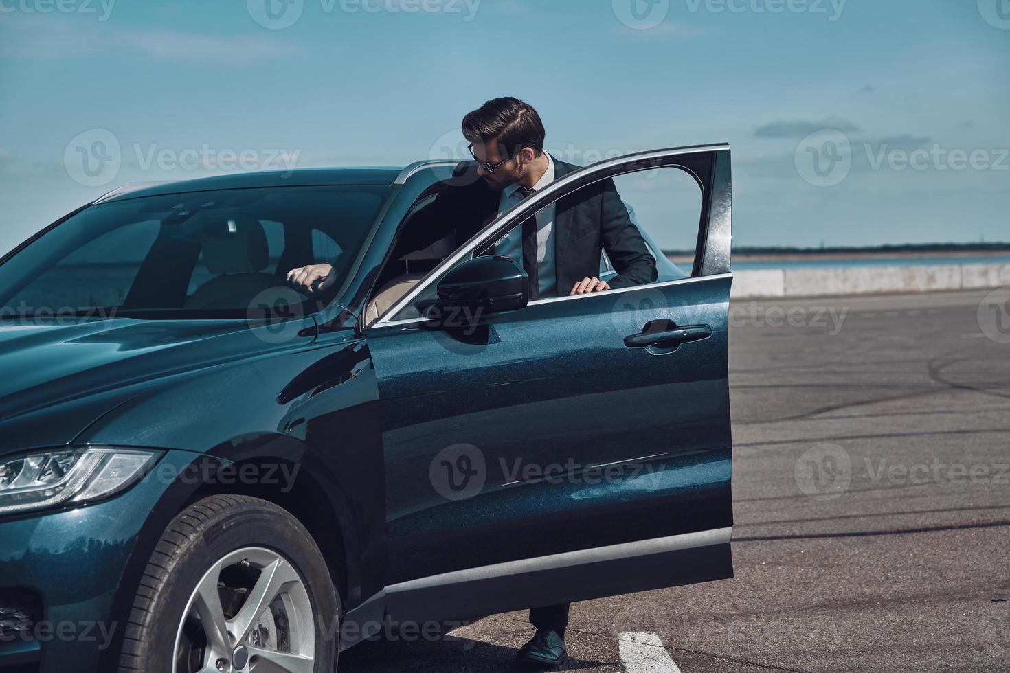 Brand new car. Handsome young businessman entering his car while standing outdoors photo