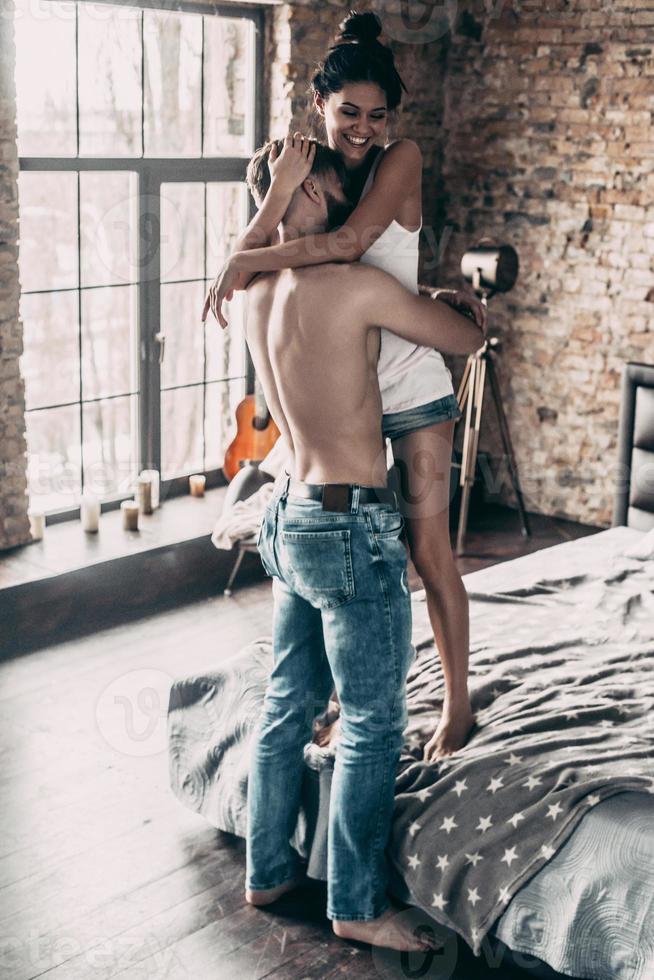 pareja feliz. toda la longitud de los jóvenes que pasan tiempo en casa mientras una hermosa chica mantiene los brazos alrededor de un hombre sin camisa y sonríe foto