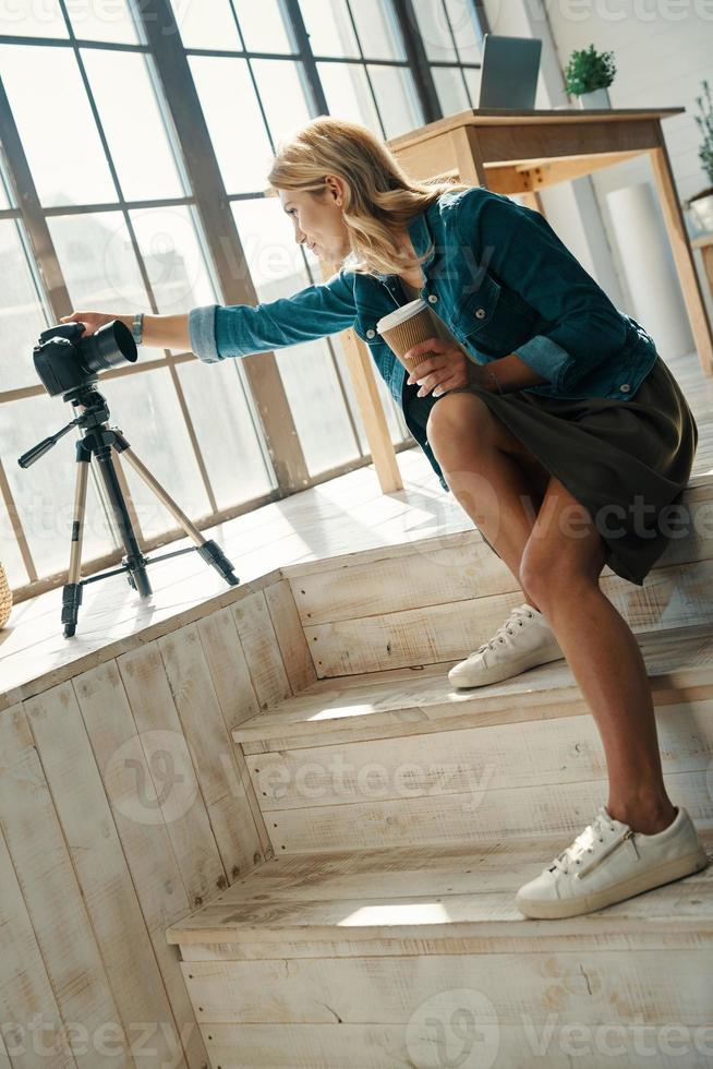 Beautiful young woman in casual clothing adjusting equipment while working in front of digital camera photo
