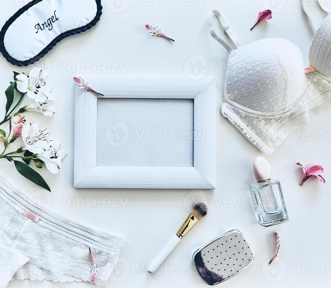Soft sensuality. High angle shot of lingerie, sleep mask, perfume, photo frame, beauty products and flowers lying against white background