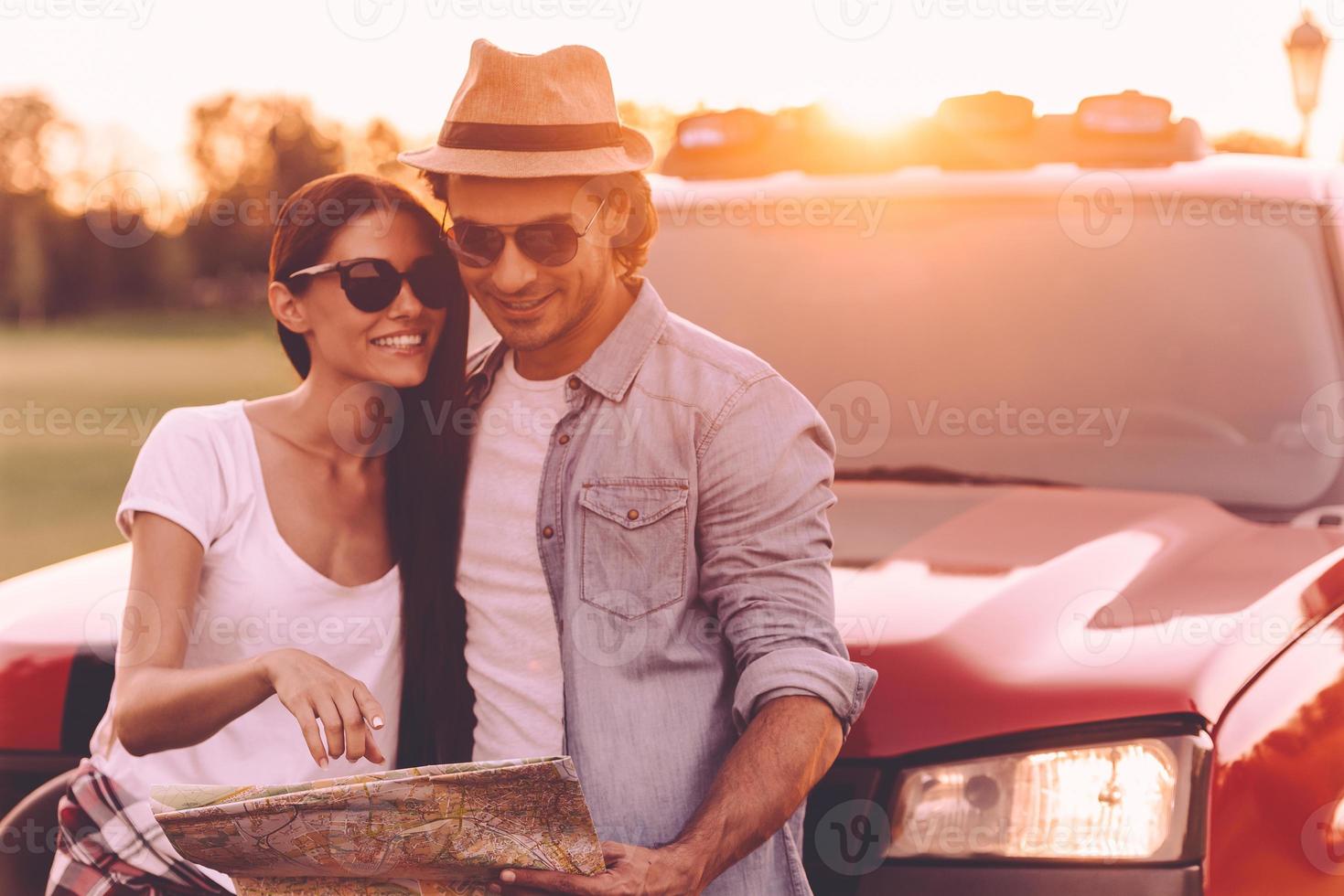 We should see this place. Beautiful young couple bonding to each other and leaning at their pick-up truck while examining map together photo