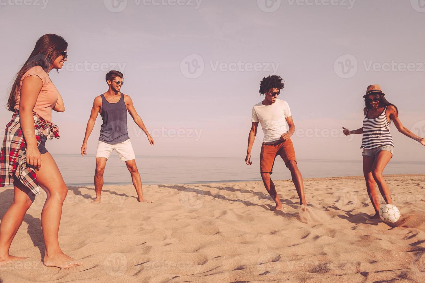 Enjoying time with friends. Group of cheerful young people playing with soccer ball on the beach with sea in the background photo