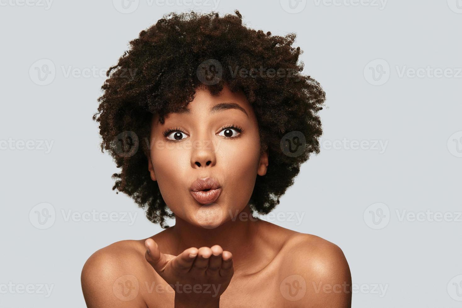 Catch  Beautiful young African woman blowing a kiss while standing against grey background photo