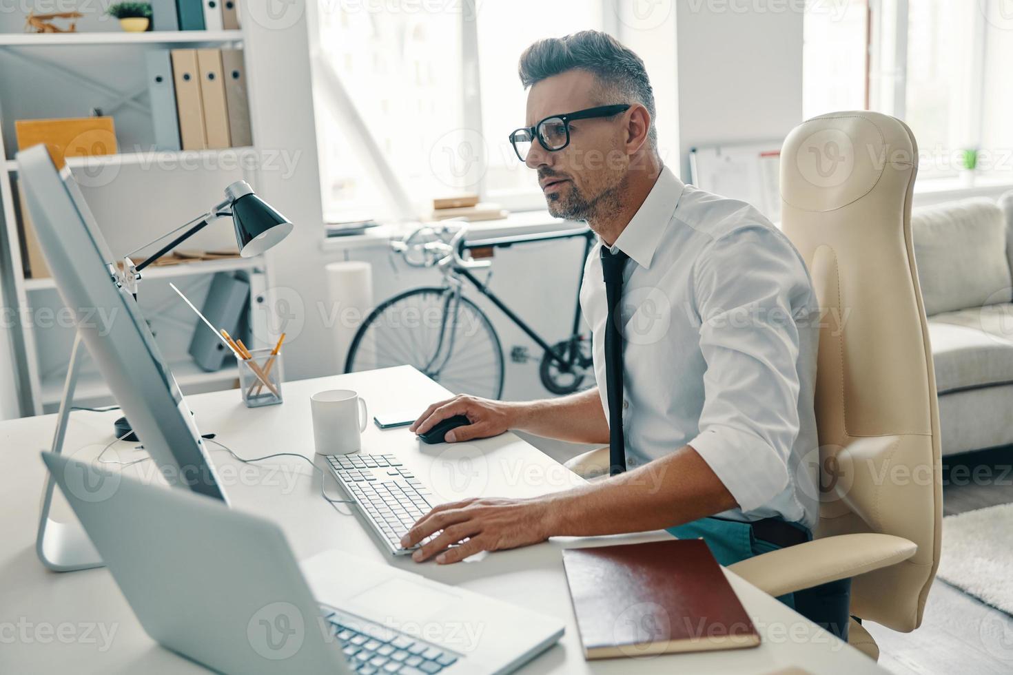 Putting ideas into something real. Thoughtful young man in shirt and tie working using computer while sitting in the office photo