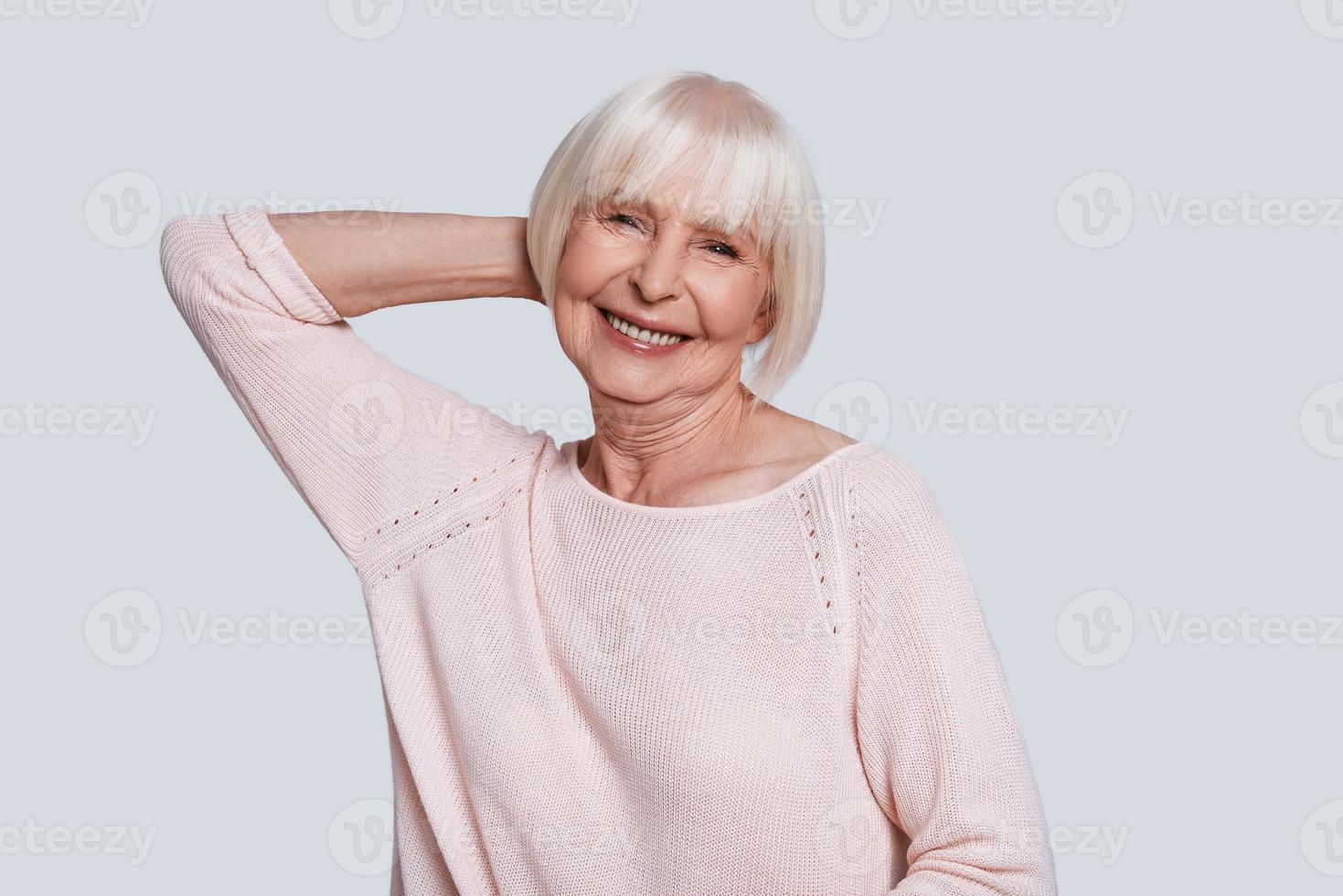 Simply happy. Beautiful senior woman looking at camera and smiling while standing against grey background photo