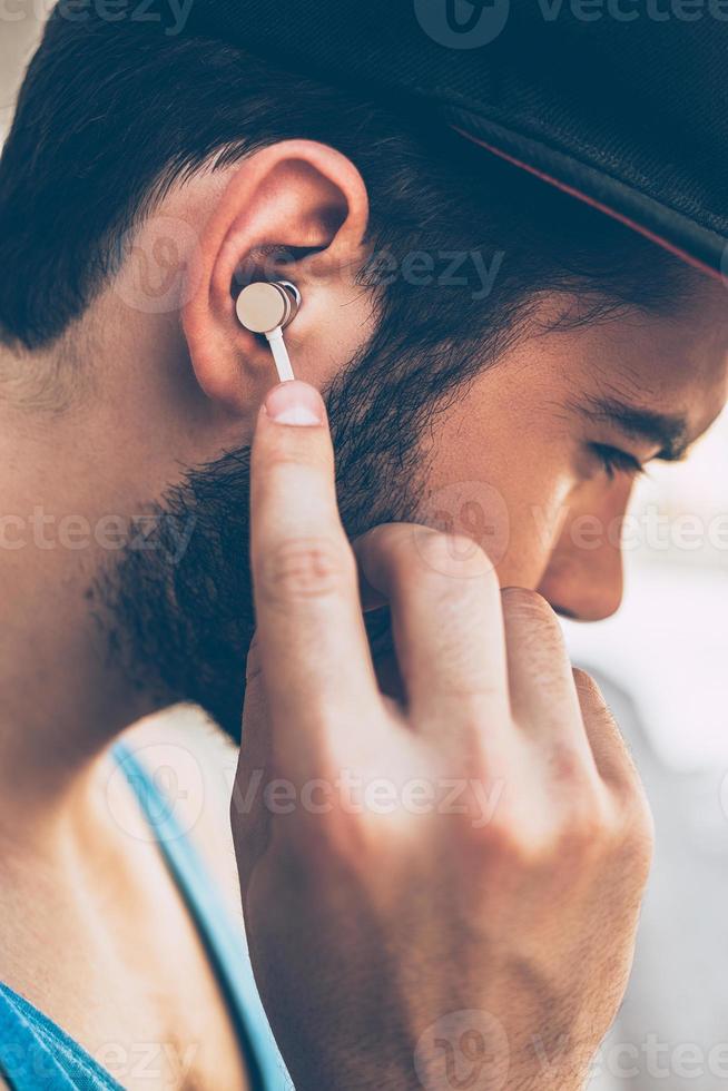 Enjoying his favorite music. Close-up of young man adjusting his headphones while standing outdoors photo